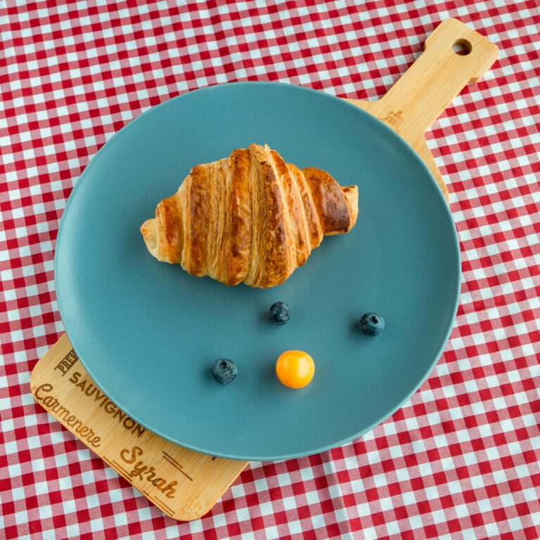 A croissant with blueberries and physalis on a stylish plate against a rustic checkered backdrop.